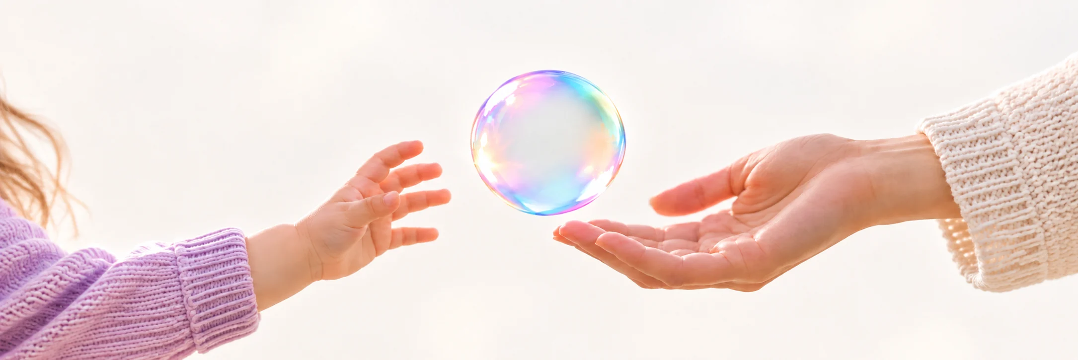 Una mano de niña se acerca a una burbuja que una mano adulta le ofrece